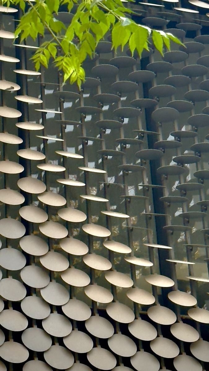 Layered disc screen facade with foliage in the foreground