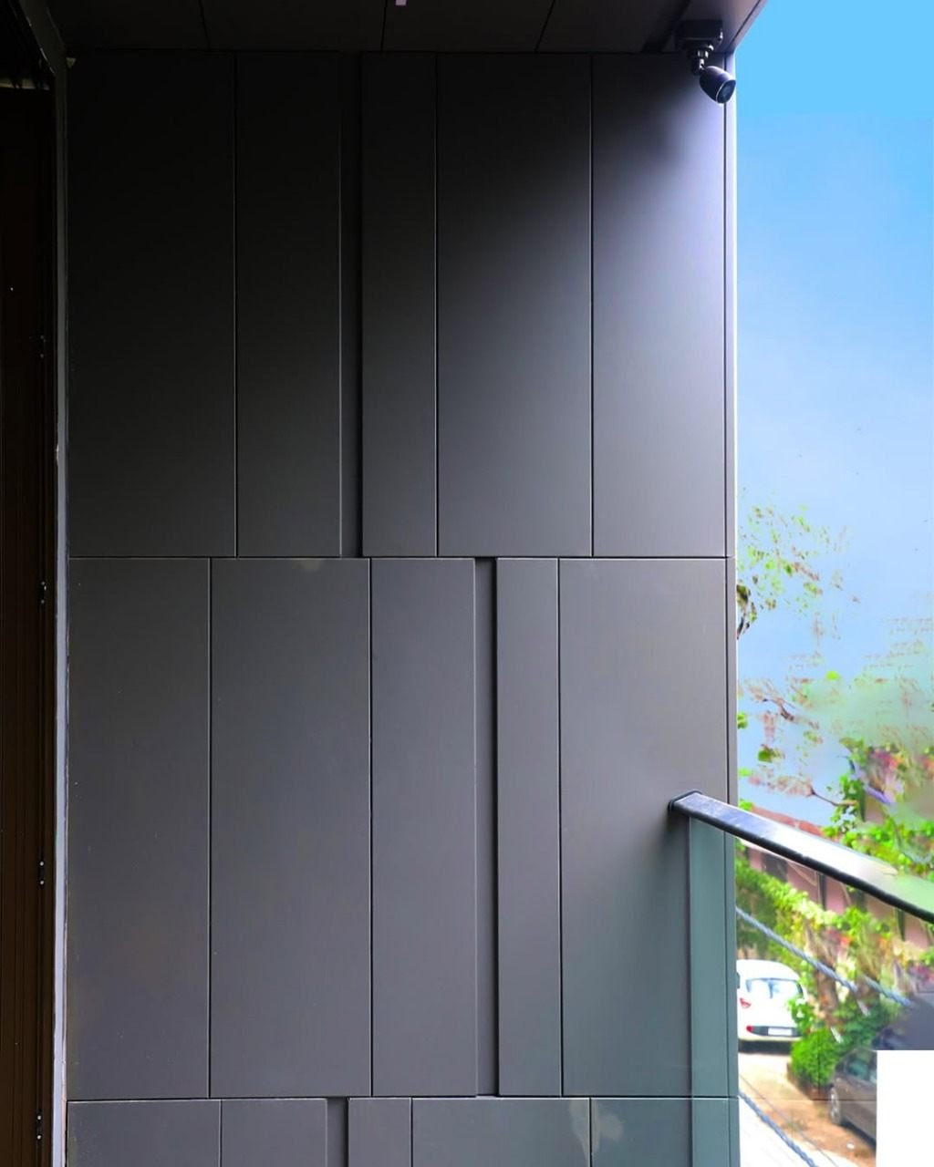 Matte charcoal ACP cladding detail with vertical panel joints beside a glass balustrade